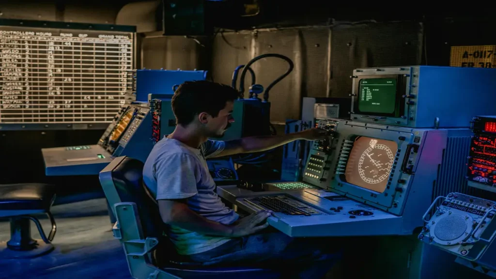 Man operating advanced control panels in a dimly lit monitoring room.