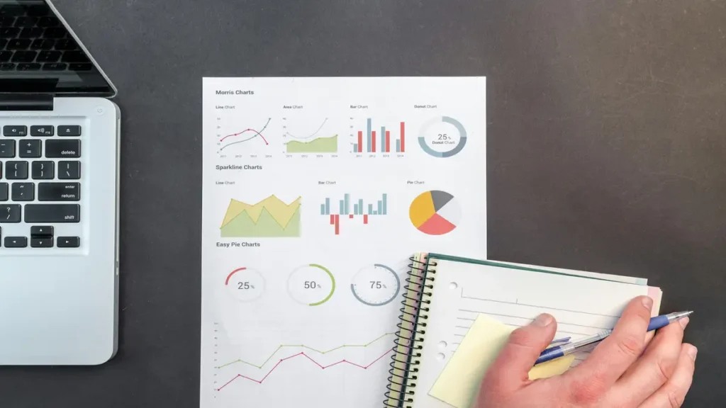 Printed analytics charts beside a laptop and notebook for data review