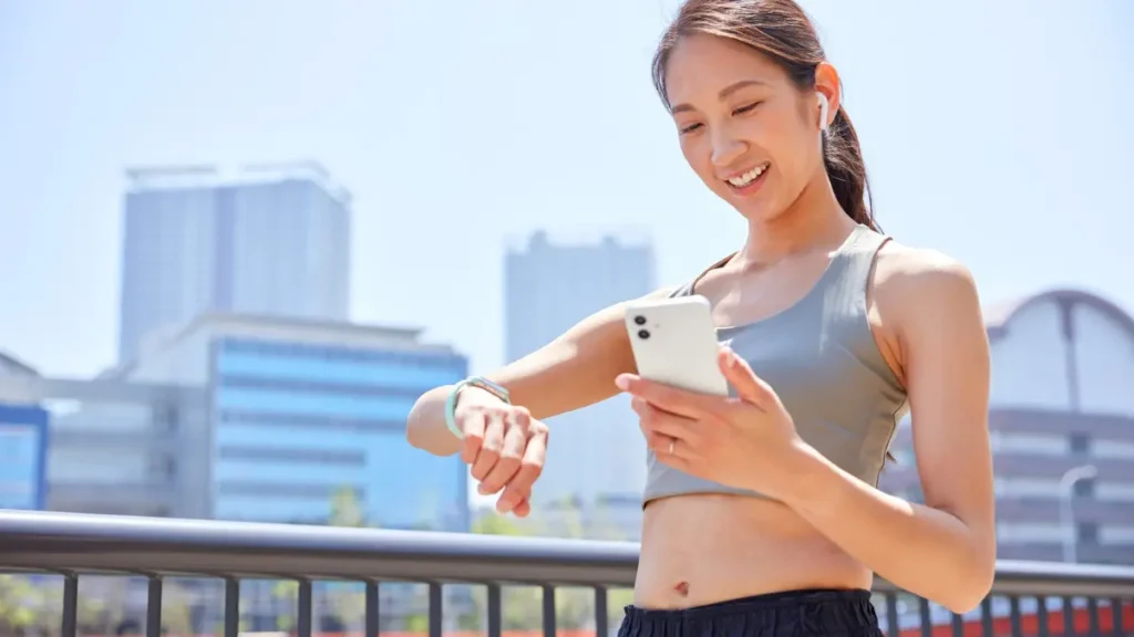 A smiling woman using wearable tech and a smartphone outdoors, reflecting modern financial tracking tools.